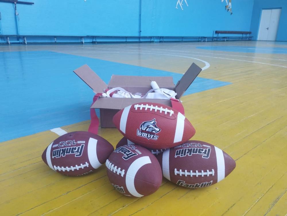 Коробка з спортивним інвентарем біля якої лежать м1ячі для американського футболу